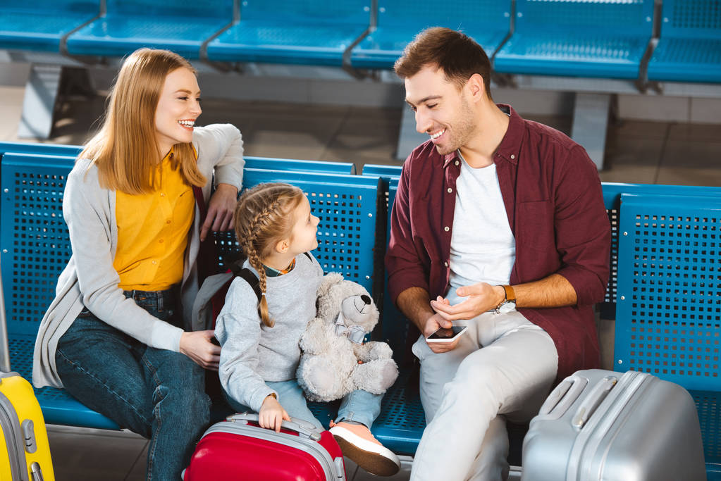 pai alegre sorrindo com a filha perto de malas e esposa no salão de partida
 - Foto, Imagem