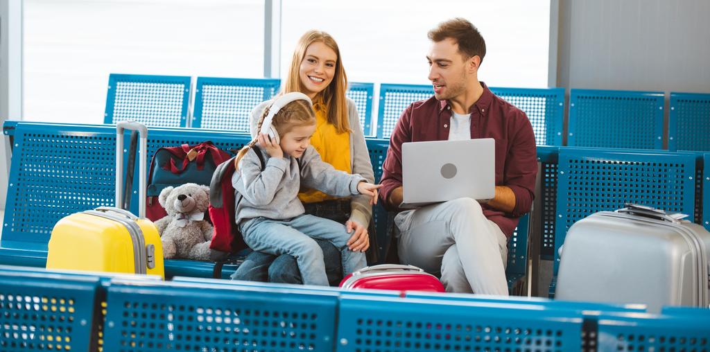 schattige dochter wijzen met de vinger naar de laptop terwijl u zit in de buurt van papa en mama in luchthaven  - Foto, afbeelding