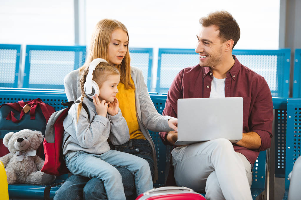 femme attrayante parlant au mari avec ordinateur portable près de la fille dans les écouteurs à l'aéroport
  - Photo, image