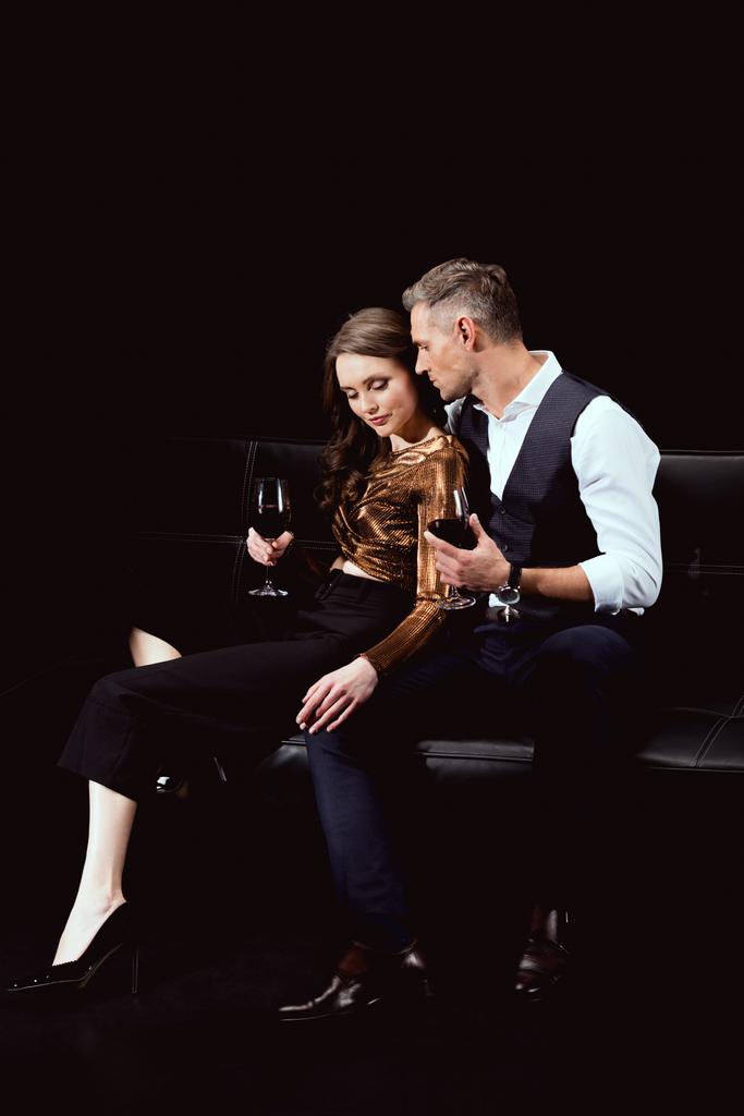 bella coppia romantica seduta sul divano con bicchieri di vino rosso isolato su nero
 - Foto, immagini