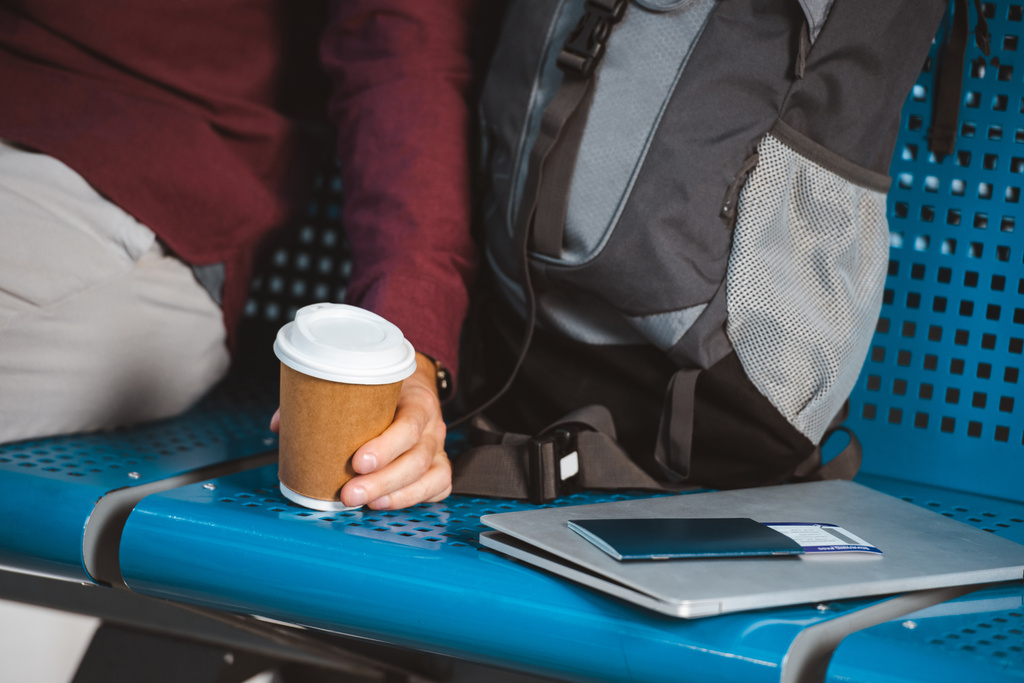 vista ritagliata dell'uomo che tiene la tazza di carta vicino allo zaino laptop e passaporto con biglietto aereo
 - Foto, immagini