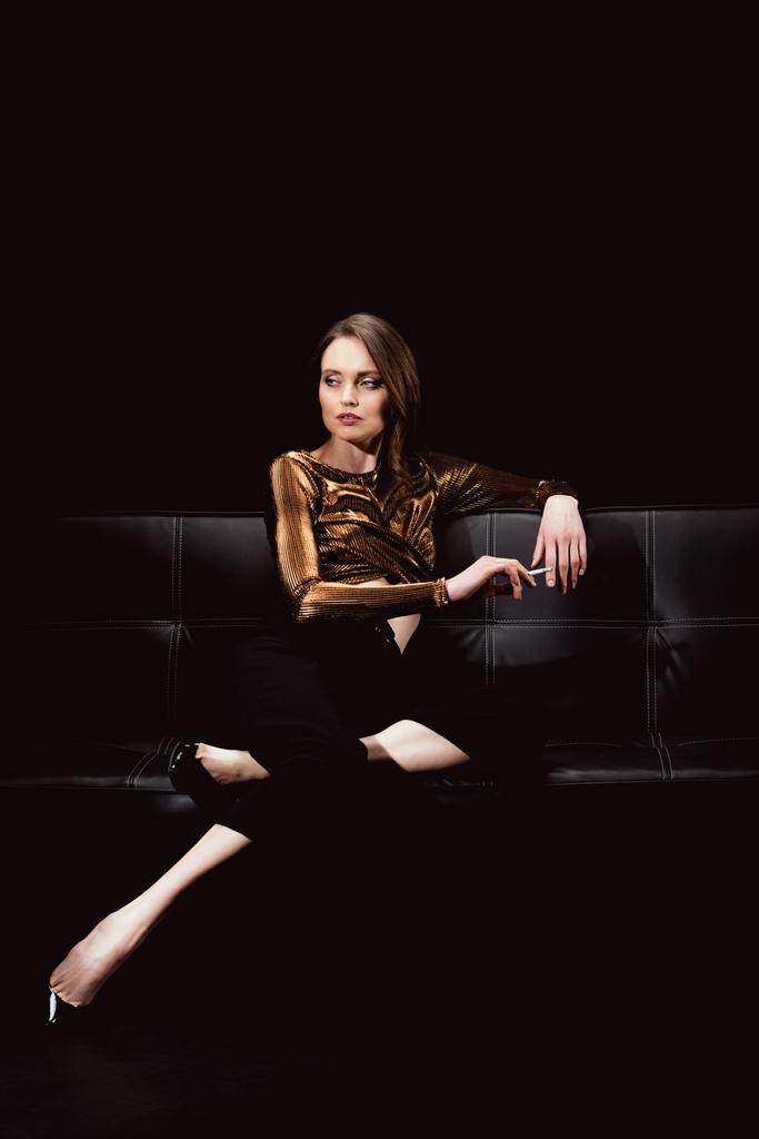 piękna glamorous kobieta siedzi na kanapie i palenia papierosów na czarnym tle - Zdjęcie, obraz