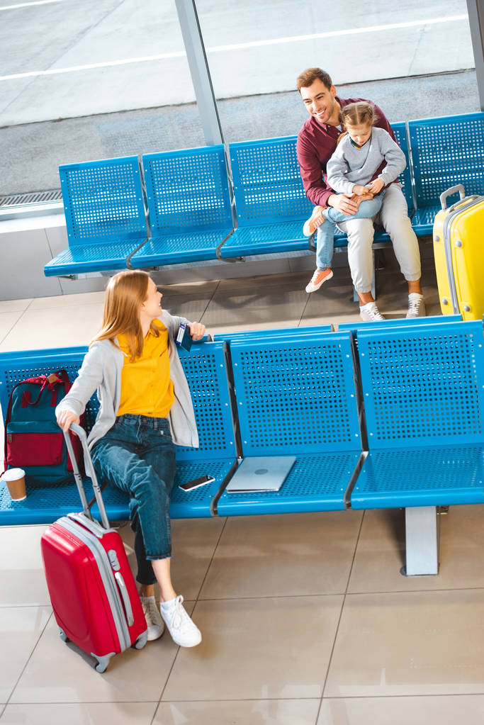 happy father sitting with daughter in airport near woman with luggage  - Photo, Image