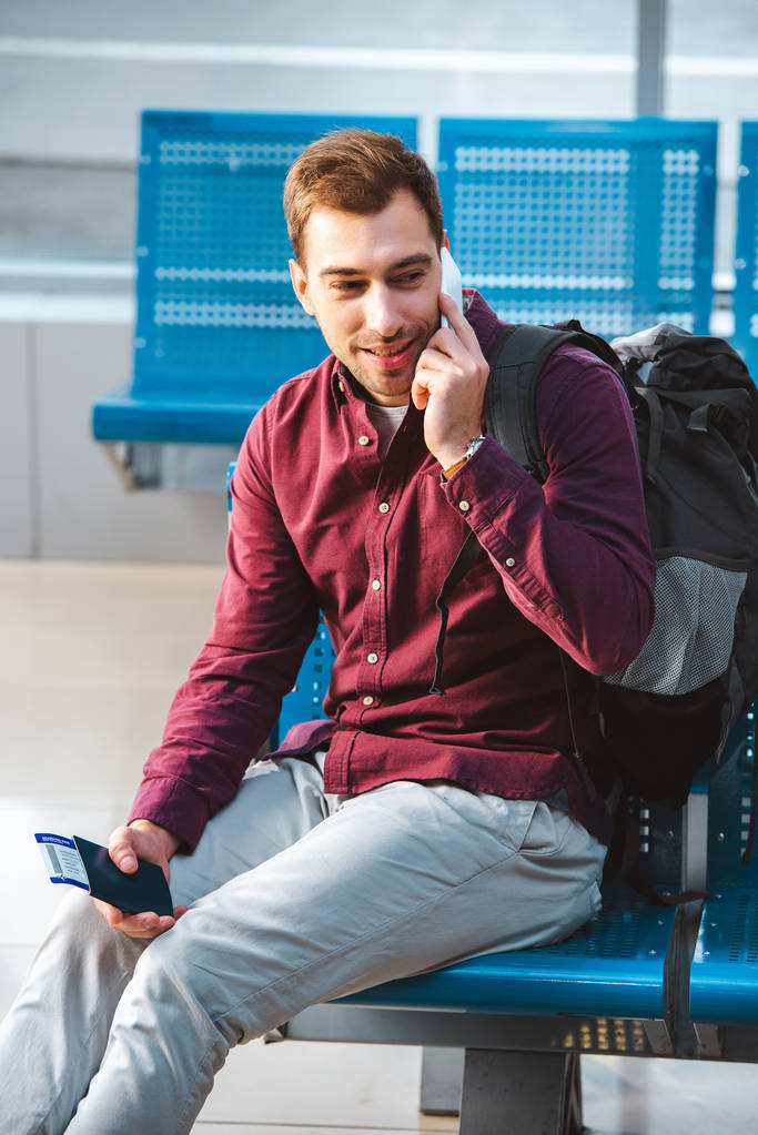 komea mies puhuu älypuhelimella ja hymyilee istuessaan lähtöaulassa
 - Valokuva, kuva