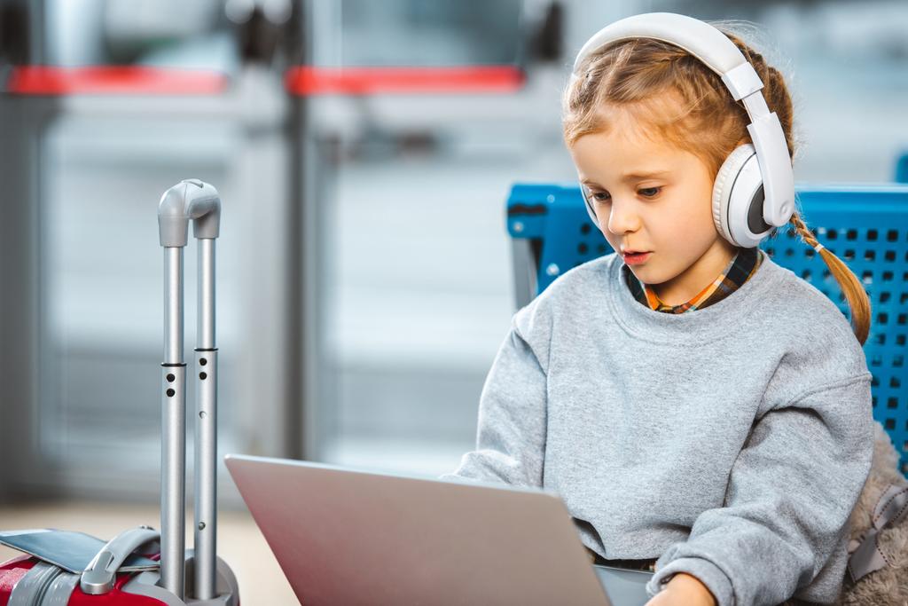 lindo niño en los auriculares con ordenador portátil en el aeropuerto
  - Foto, Imagen