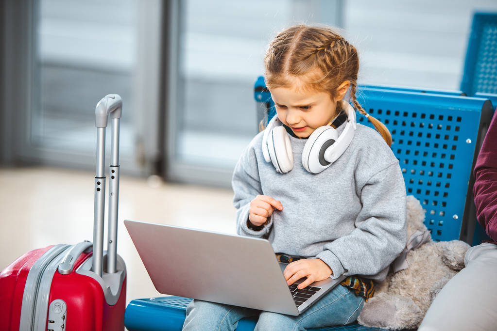 cute child in headphones using laptop in airport  - Photo, Image