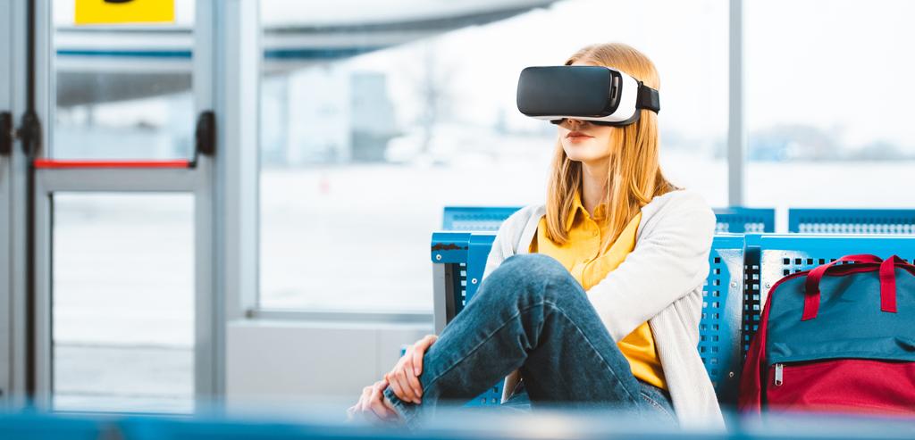 Nainen yllään virtuaalitodellisuus kuulokkeet odottaessaan lähtöä lounge lähellä reppu
 - Valokuva, kuva