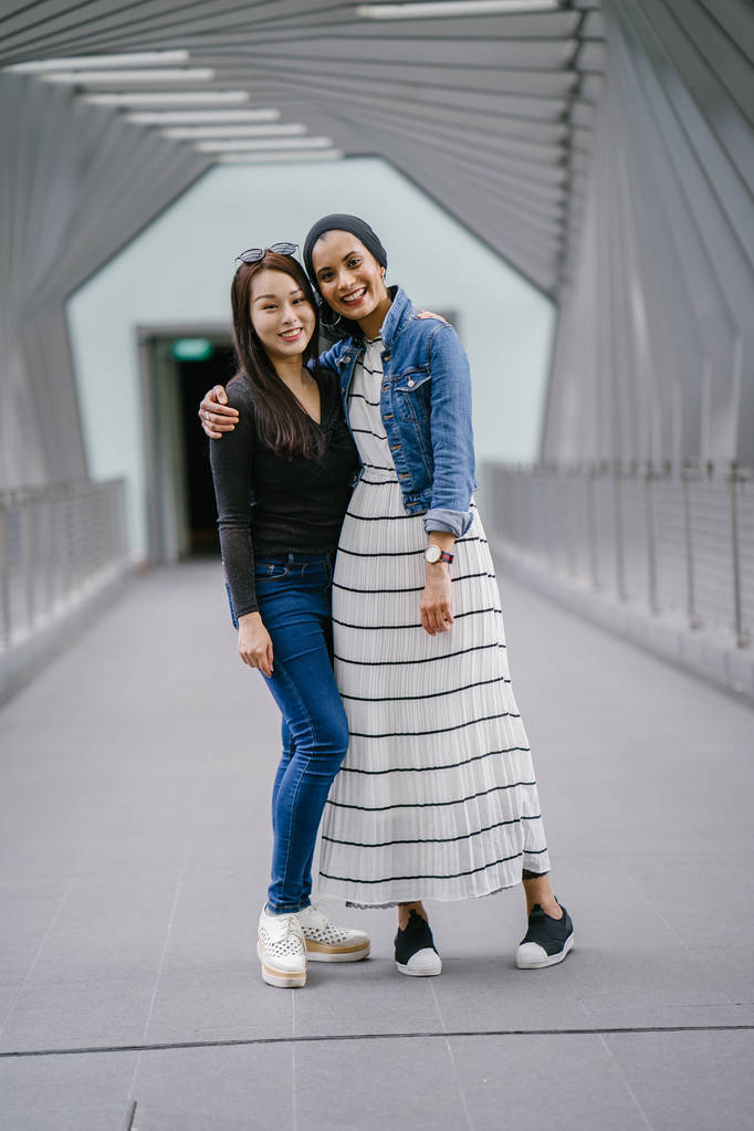 Deux amis de différentes origines ethniques sur un pont pendant la journée. L'une est une musulmane malaise et l'autre est d'origine chinoise. Ils sont jeunes, énergiques et attirants.. - Photo, image