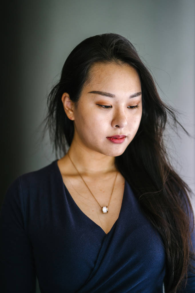 Een close-up bedrijfs portret van een zelfverzekerde, jonge, mooie en zelfverzekerde Aziatische vrouw in een blauwe jurk. Ze heeft lang haar en glimlacht zachtjes voor haar hoofdschot - Foto, afbeelding