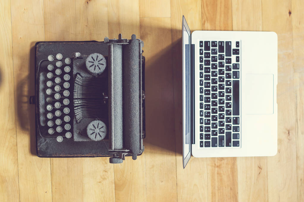 стара старовинна друкарська машинка з пиловим покриттям з аркушем білого паперу біля сучасного ноутбука на фоні книжкової шафи. сучасні технології та старовинні прилади
 - Фото, зображення