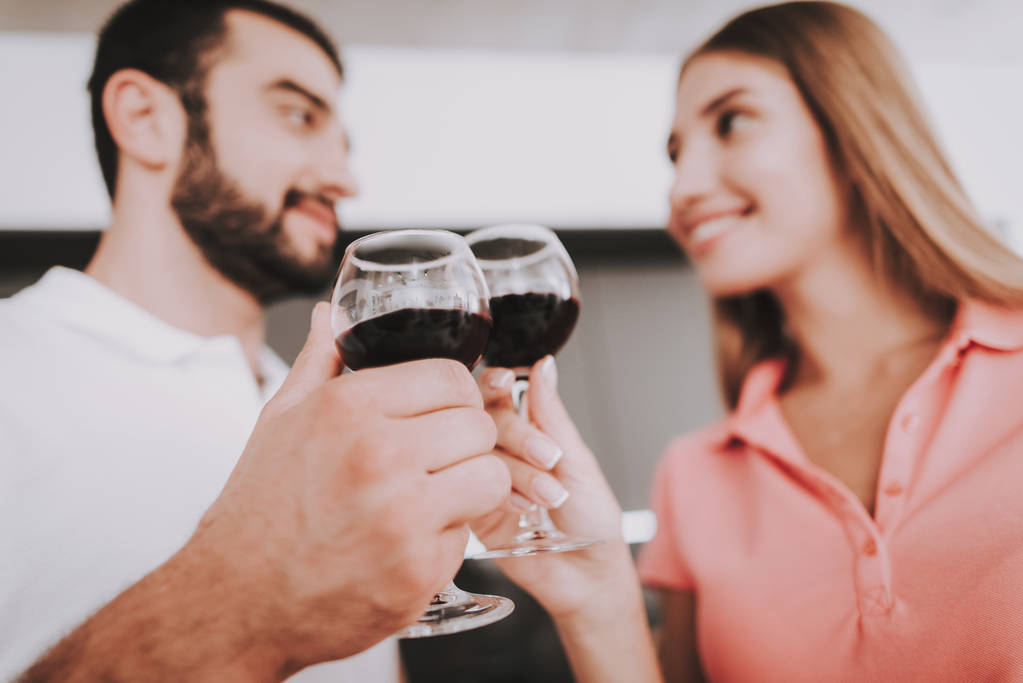 Чоловік і жінка п'ють вино на кухні. Вони тримають келихи вина в руках. Вони дивляться один на одного і посміхаються. Вони на кухні вдома
. - Фото, зображення