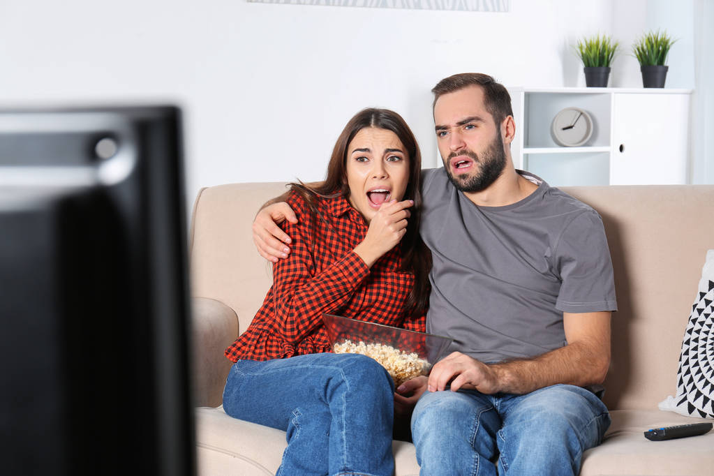 Молода пара дивиться телевізор на дивані вдома
 - Фото, зображення