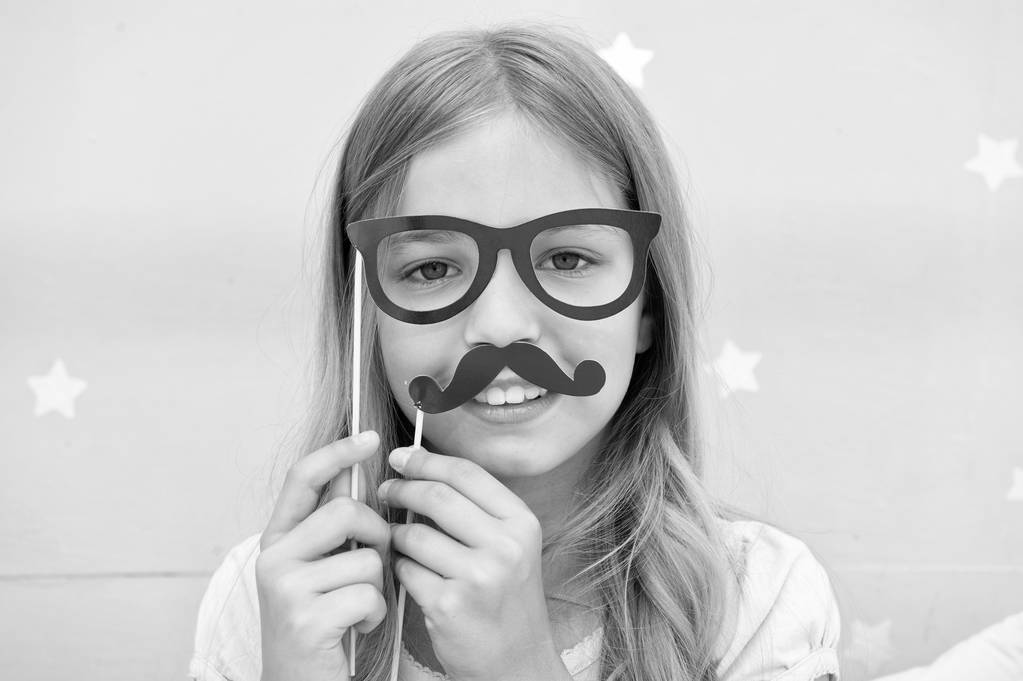 Girl pose with photo booth props glasses and mustick in bedroom. Κορίτσι με γυαλιά για πάρτι. Το παιδί μιμείται τον ανδρισμό ή θέλει να μοιάζει με τον πατέρα της. Παιδί με μουστάκι και γυαλιά - Φωτογραφία, εικόνα