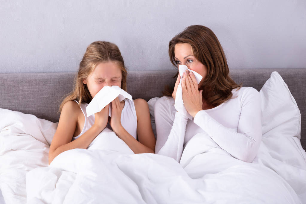 Matka i córka cierpi na zimno dmuchanie jej nos chusteczką na łóżku - Zdjęcie, obraz