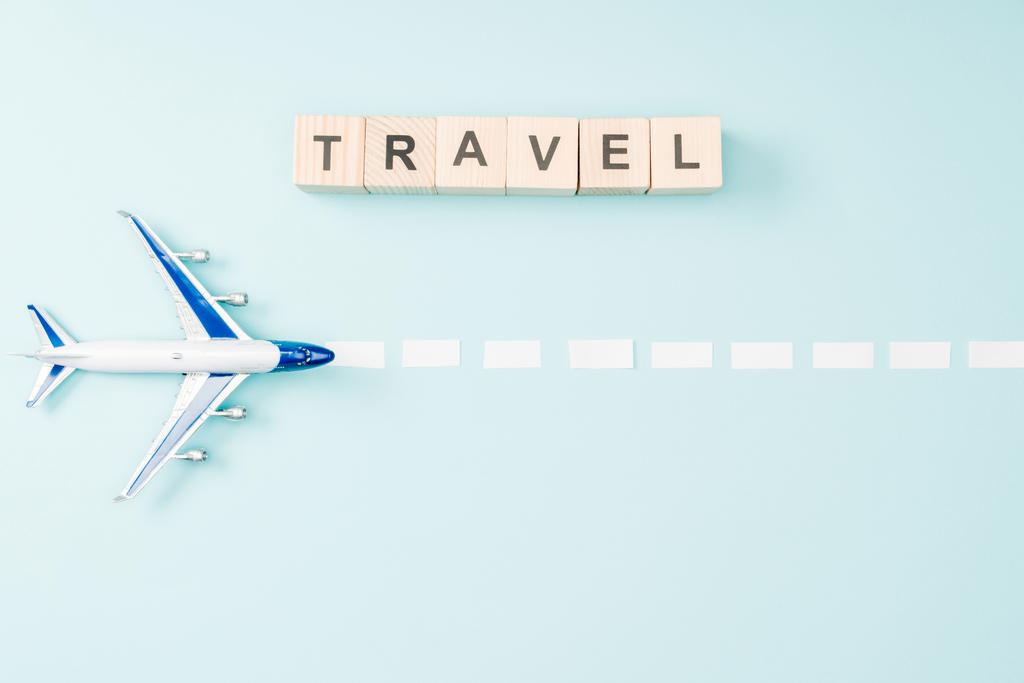 Draufsicht auf Spielzeugflugzeug, gestrichelte Linie und Holzwürfel mit Reiseschrift auf blauem Hintergrund - Foto, Bild