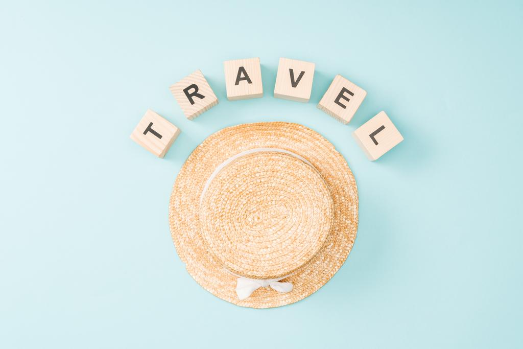 κάτοψη του ξύλινα κύβοι με γράμματα ταξίδια και ψάθινο καπέλο σε μπλε φόντο - Φωτογραφία, εικόνα