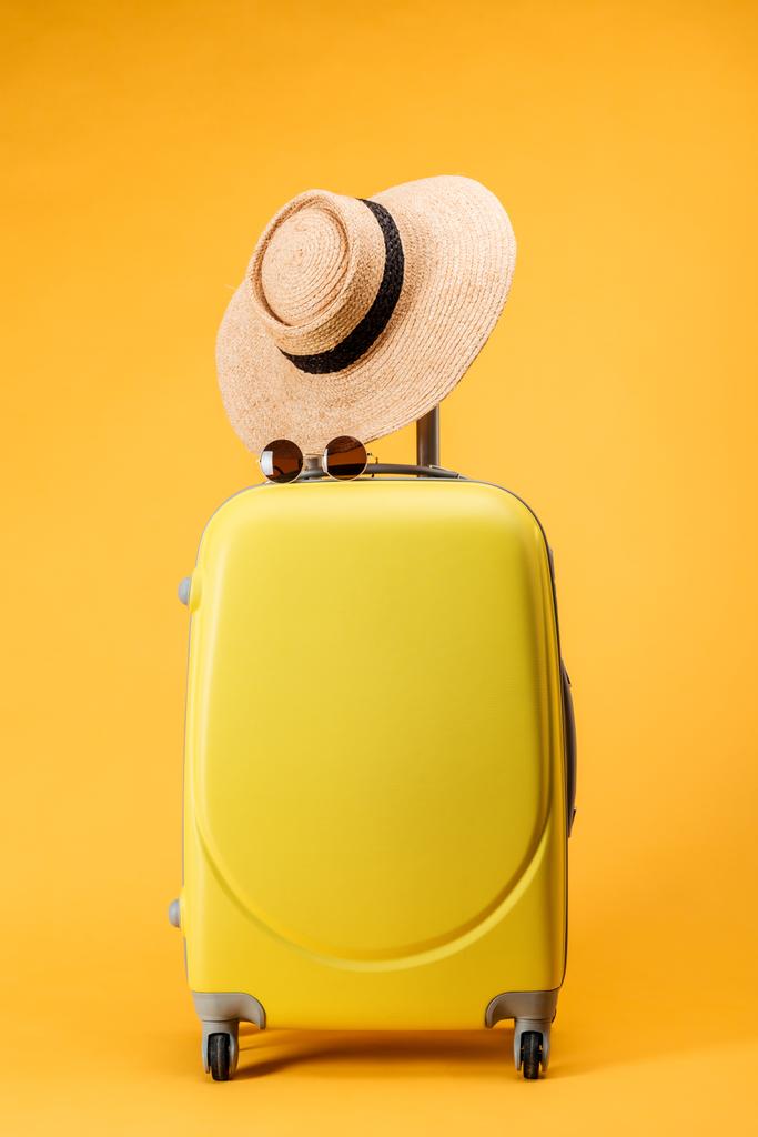 bolsa de viaje con ruedas, sombrero de paja y gafas de sol sobre fondo amarillo
 - Foto, imagen