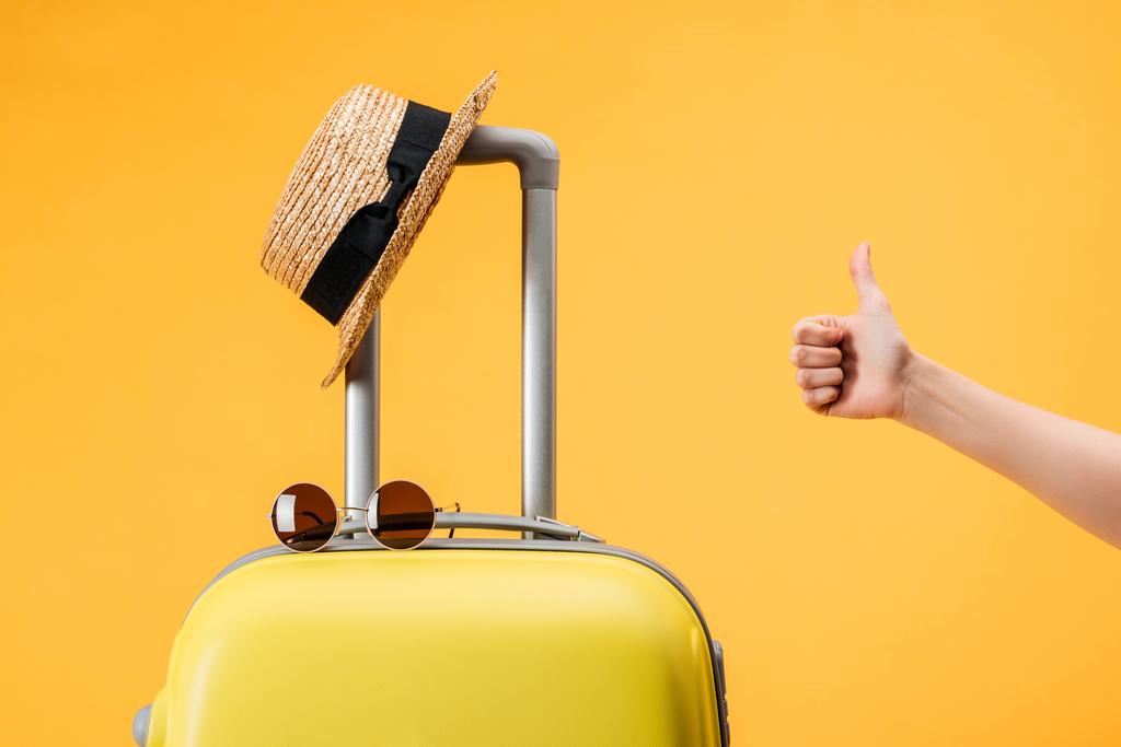 przycięte widzenia kobieta robi kciuk gest w pobliżu torba podróżna, słomkowy kapelusz i okulary przeciwsłoneczne, żółty - Zdjęcie, obraz