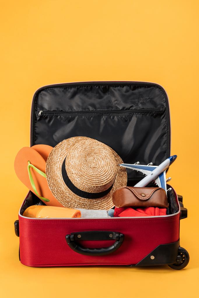Spielzeugflugzeug, Strohhut, Flip-Flops und Kleidung in Reisetasche auf gelbem Hintergrund - Foto, Bild