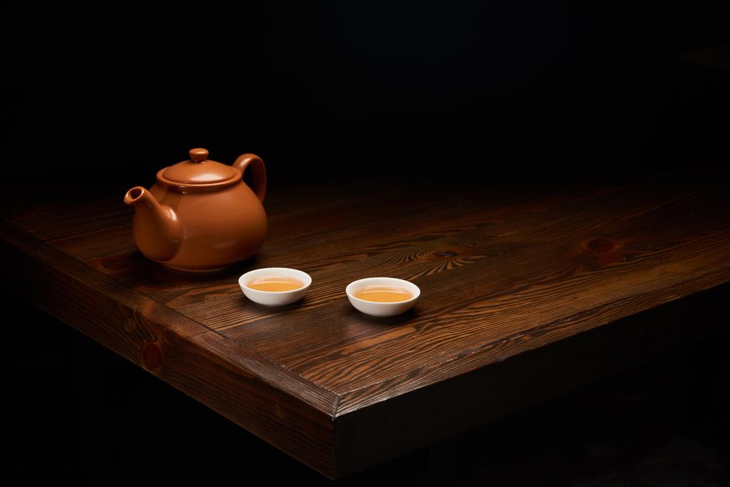 pot avec thé chinois traditionnel et tasses sur table en bois isolé sur noir
 - Photo, image