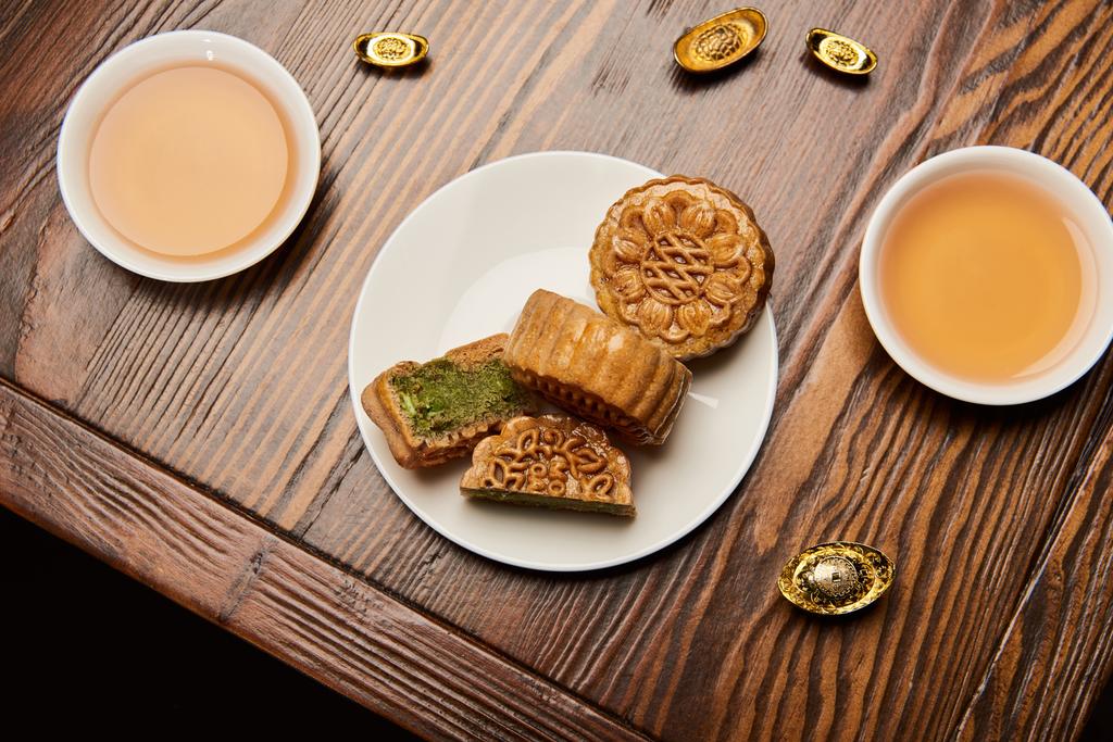 tartas de luna tradicionales con tazas de té y lingotes de oro en la mesa de madera
 - Foto, Imagen