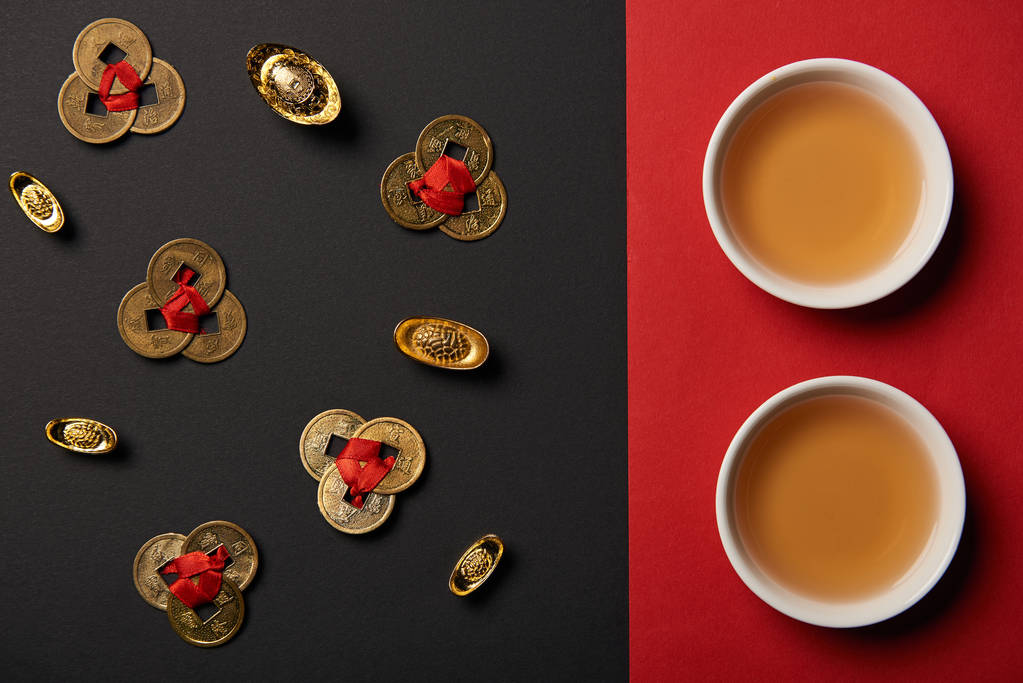bovenaanzicht van thee bekers en feng shui munten op rode en zwarte achtergrond  - Foto, afbeelding
