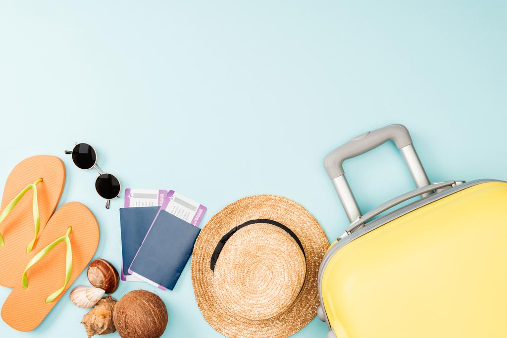 Widok z góry z słomkowy kapelusz, kokos, flip flops, muszle, Okulary przeciwsłoneczne, paszporty, bilety lotnicze i torba podróżna na niebieskim tle - Zdjęcie, obraz