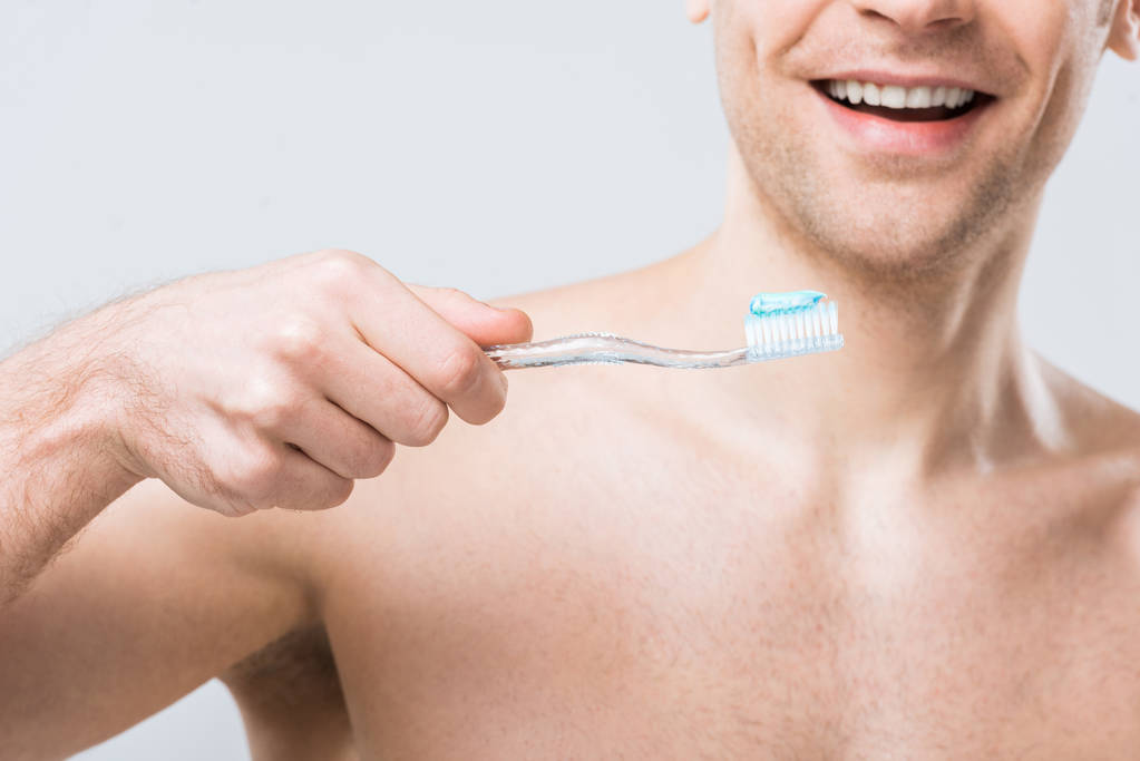 przycięte widzenia uśmiechnięty mężczyzna trzymając szczoteczkę do zębów pastą, na szarym tle - Zdjęcie, obraz