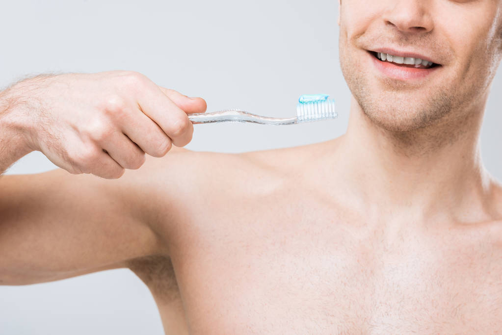 obcięty widok mężczyzny trzymającego pasty do zębów, na szarym tle elektryczna szczoteczka do zębów - Zdjęcie, obraz