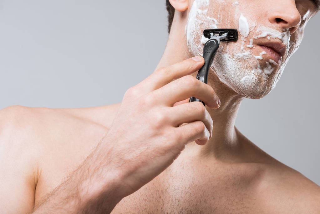 bijgesneden weergave van man schuim op gezicht scheren met een scheermes, geïsoleerd op grijs - Foto, afbeelding