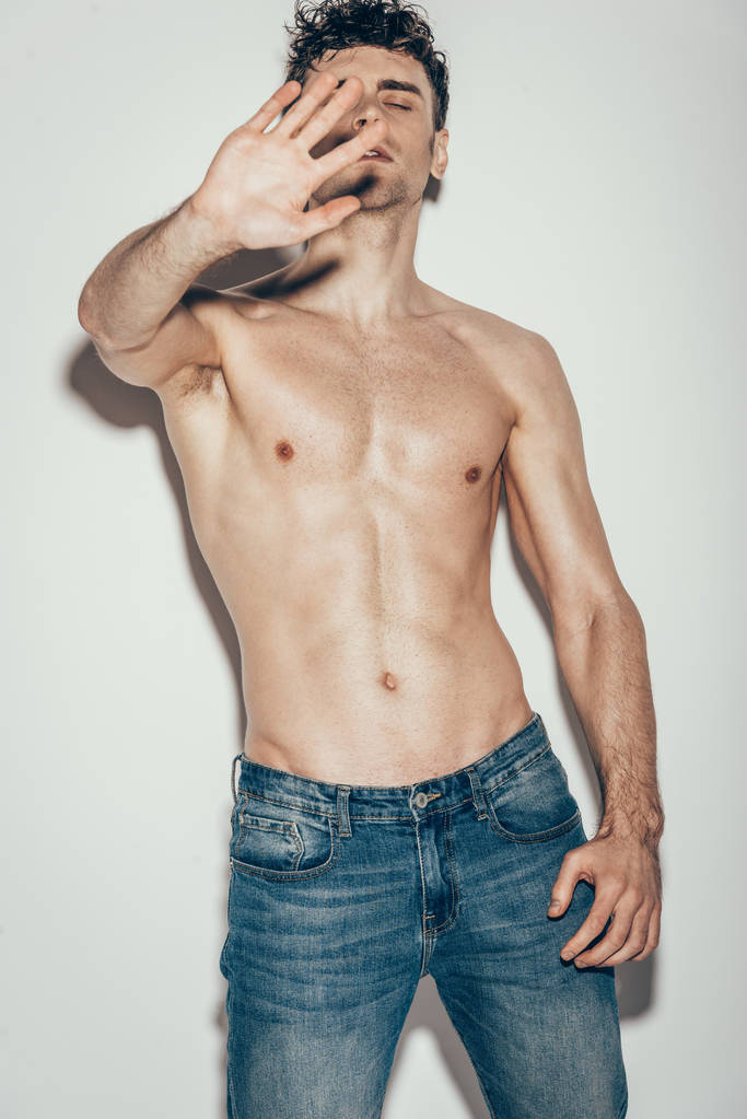 сексуальный мужчина без рубашки в джинсах жестикулирует и позирует на сером
 - Фото, изображение