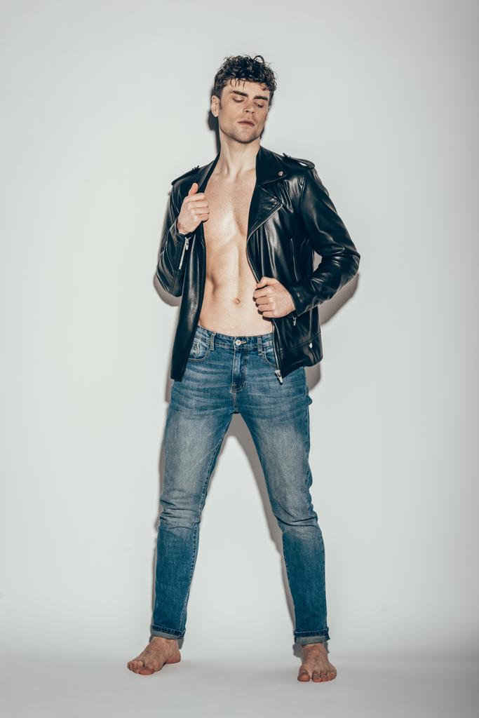 сексуальный молодой человек позирует в джинсах и черной кожаной куртке на сером
 - Фото, изображение
