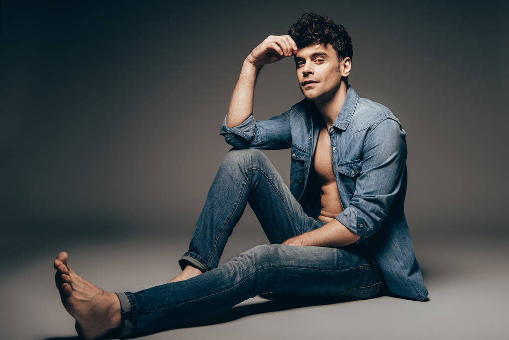 schöner junger sexy Mann posiert in Jeans-Klamotten auf dunkelgrau - Foto, Bild