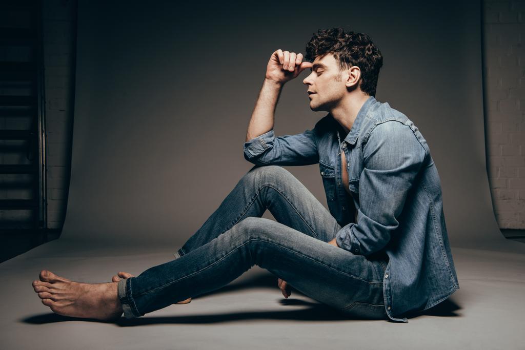 barefoot thoughtful man posing in jeans clothes on dark grey - Photo, Image