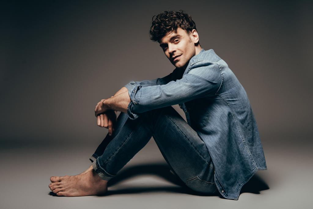 sexy descalzo hombre sentado en jeans ropa en gris oscuro
 - Foto, imagen