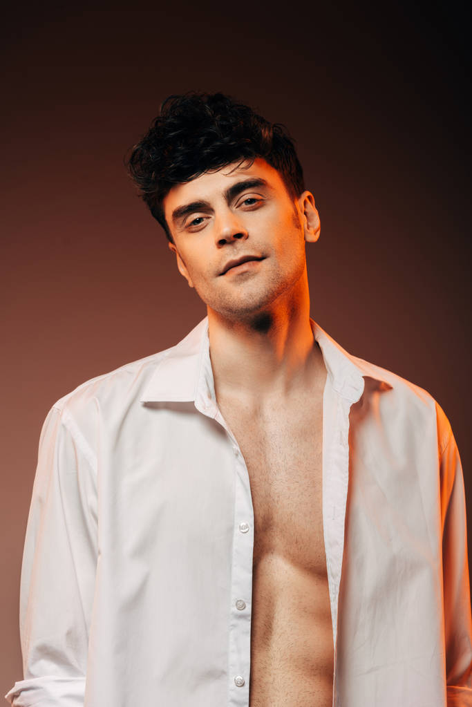 модный сексуальный мужчина позирует в белой рубашке, изолированный на коричневый
 - Фото, изображение