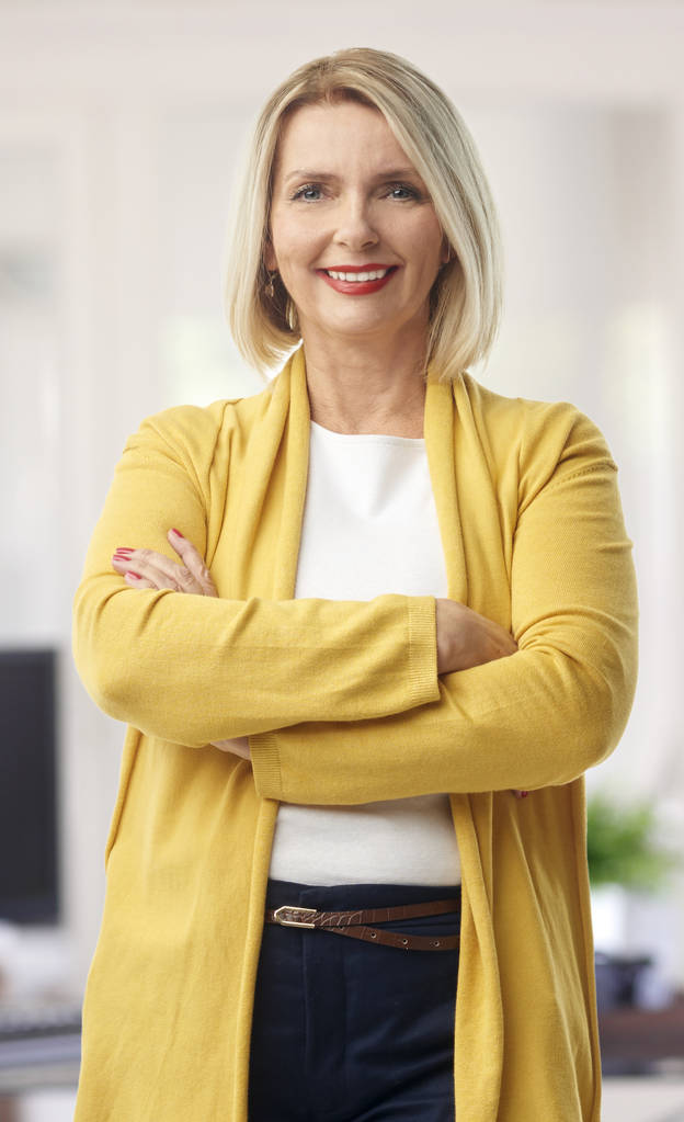 A beautiful mature sales businesswoman wearing casual clothes and smiling to you while standing with arms crossed at the office.  - Photo, Image