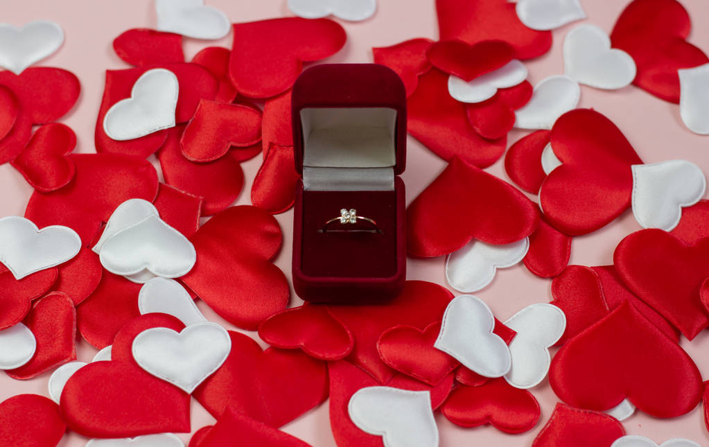 Δαχτυλίδι σε ένα κόκκινο κουτί σε ένα φόντο από καρδιές των ερυθρών και των λευκών. Γαμήλιο δαχτυλίδι στο πλαίσιο. Γάμος πρόταση έννοια, ημέρα του Αγίου Βαλεντίνου, ημέρα της γυναίκας. - Φωτογραφία, εικόνα