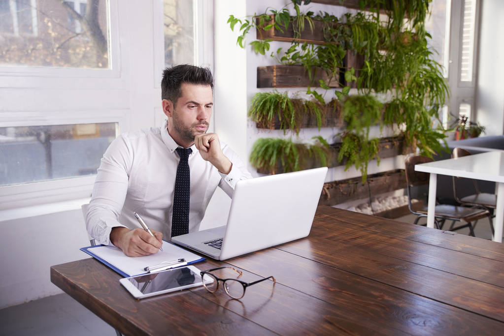 Портрет бизнесмена, задумчиво смотрящего, сидя за рабочим столом и печатая на ноутбуке
. - Фото, изображение