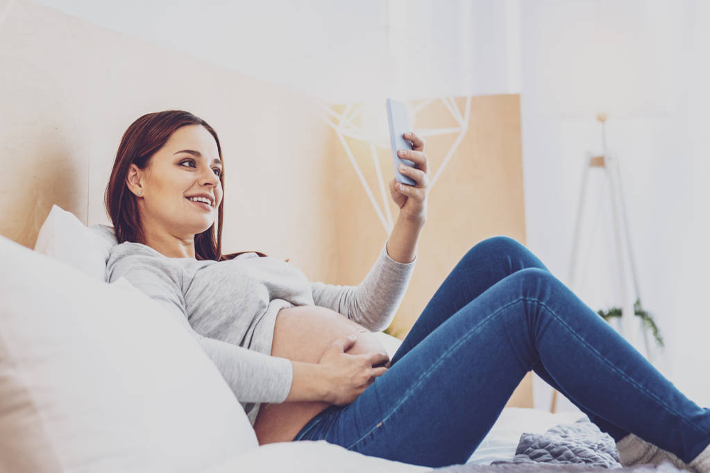 Mulher grávida alegre tomando selfie na cama
 - Foto, Imagem