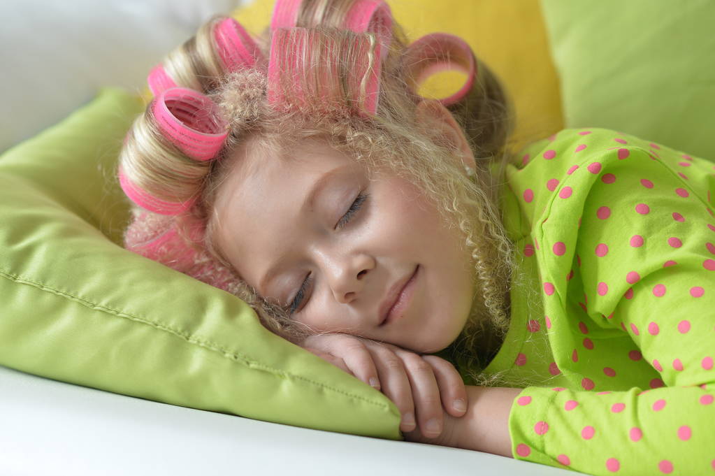 Preciosa niña con rizadores rosados durmiendo en casa
 - Foto, imagen