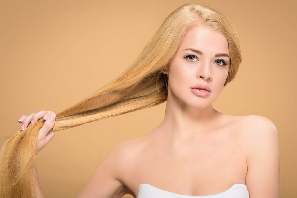 Pretty girl holding long straight hair on beige background - Photo, Image