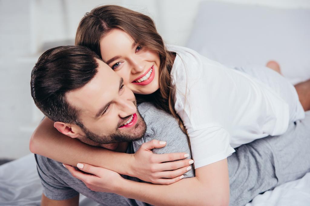 foco seletivo de jovem casal amoroso abraçando e sorrindo na cama
 - Foto, Imagem