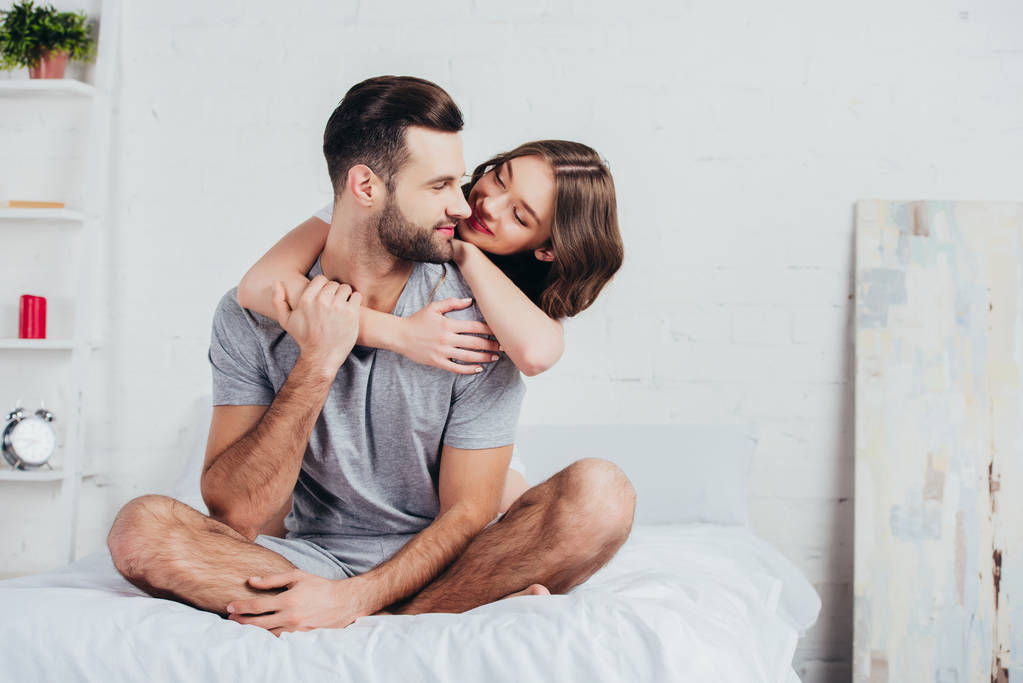 coppia adulta che abbraccia e si siede sul letto con biancheria da letto bianca
 - Foto, immagini