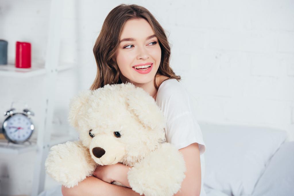 szelektív összpontosít, mosolygós nő mosolyogva, és teddy medve átölelve az ágyban - Fotó, kép