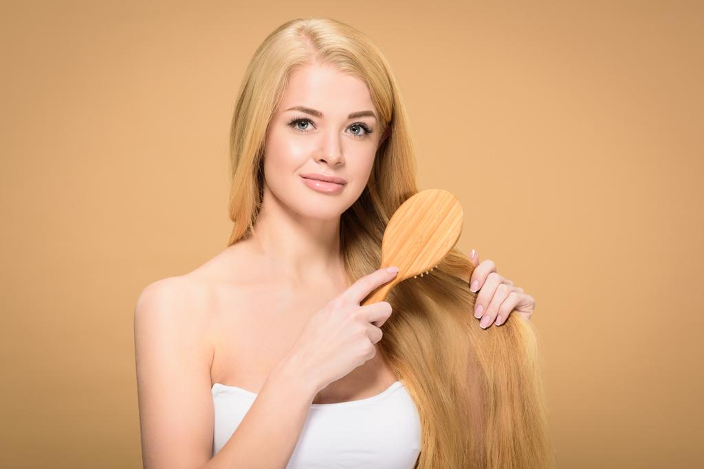 Menina loira atraente usando escova de cabelo e olhando para a câmera
 - Foto, Imagem
