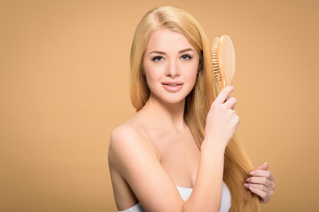 Front view of pretty blonde woman holding wooden hair brush  - Photo, Image