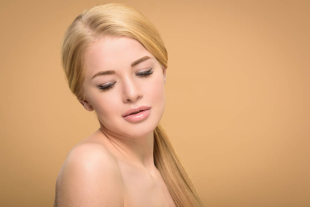 mujer rubia desnuda con el pelo largo y brillante mirando hacia abajo aislado en beige
 - Foto, Imagen