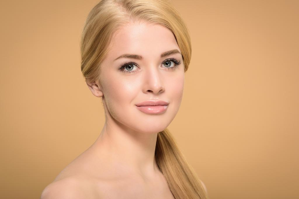 портрет привлекательной блондинки с длинными гладкими волосами, смотрящей на камеру, изолированную от бежевого
 - Фото, изображение