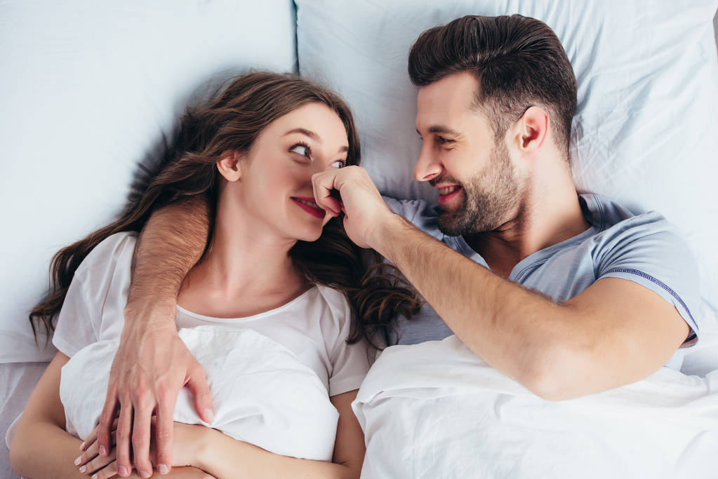 Liebender junger Mann umarmt Frau sanft im Bett und berührt Nase - Foto, Bild